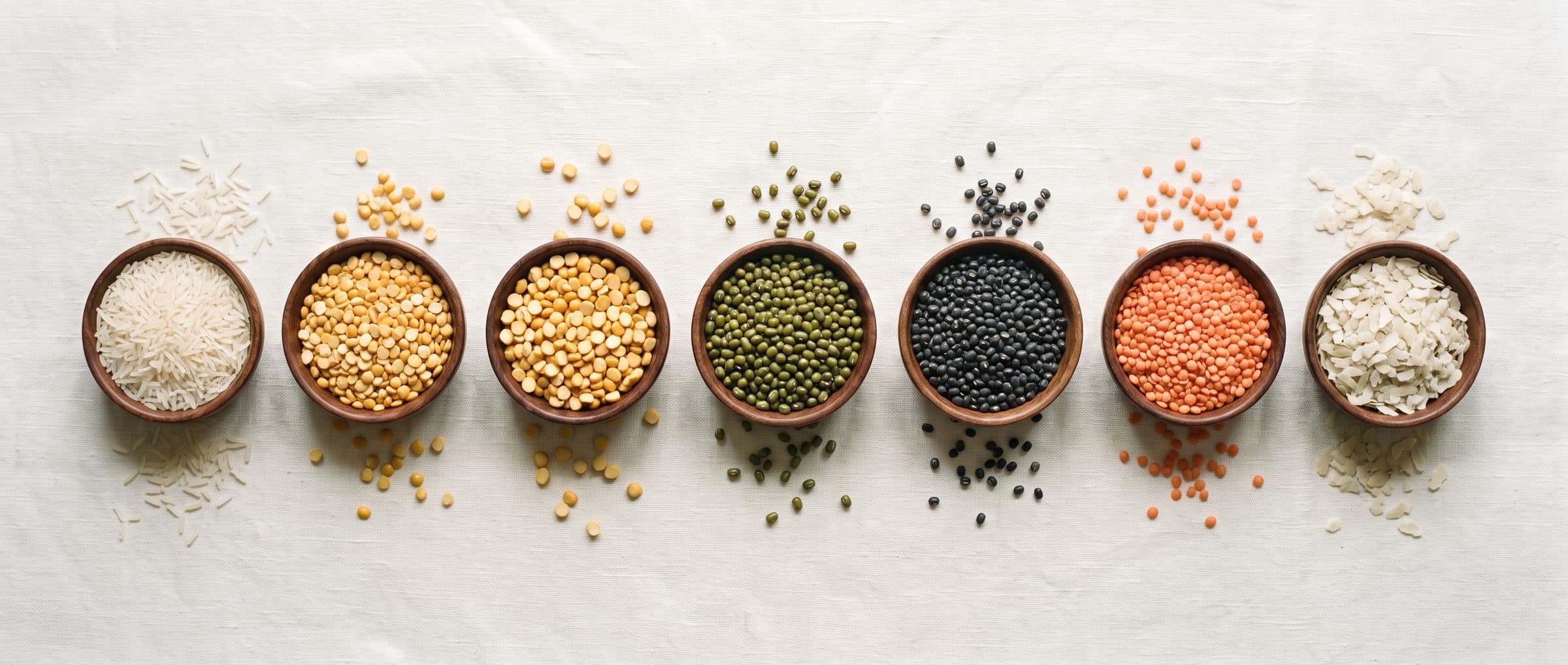 Rice, dals, pulses and flattened rice in small wooden bowls on ivory linen